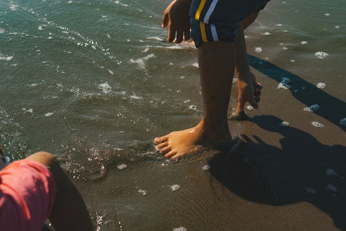 Children playing as sea water washes over their feet on a family beach holiday