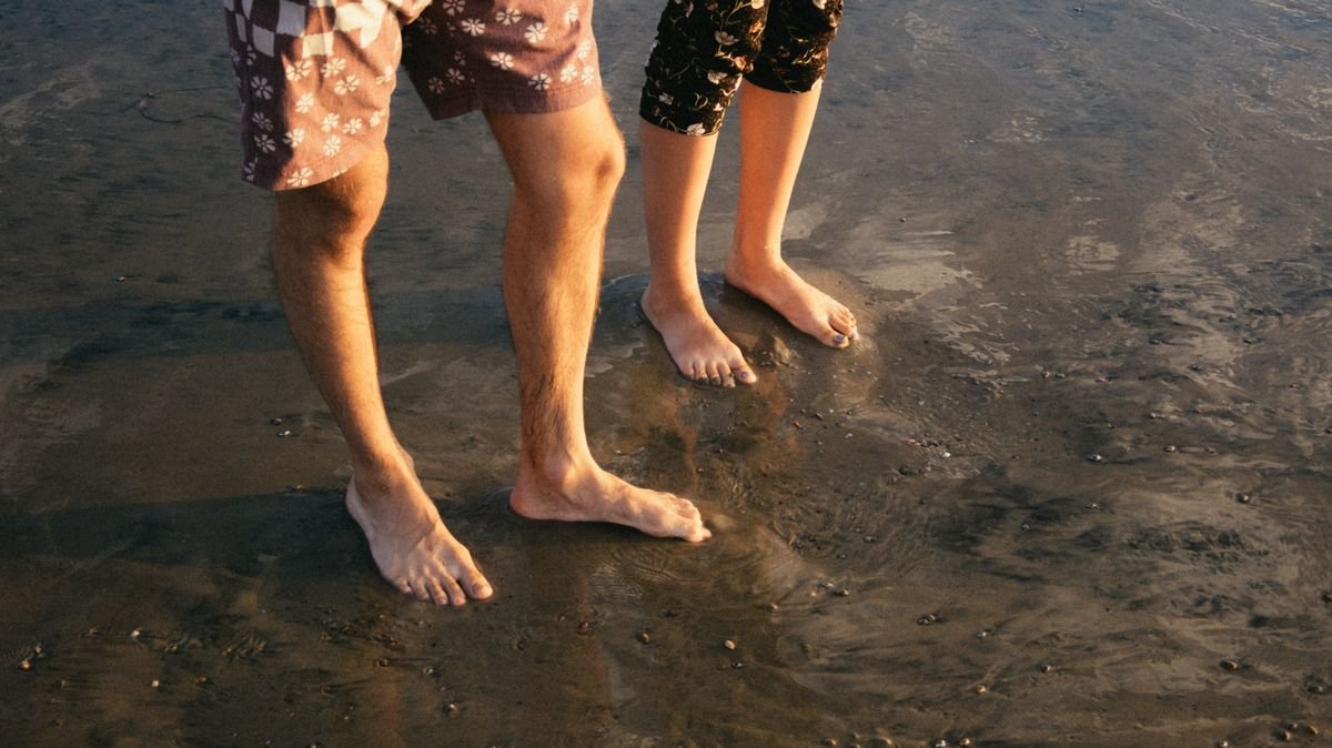 Couple standing barefoot on wet sand at the beach during sunset, on a romantic getaway